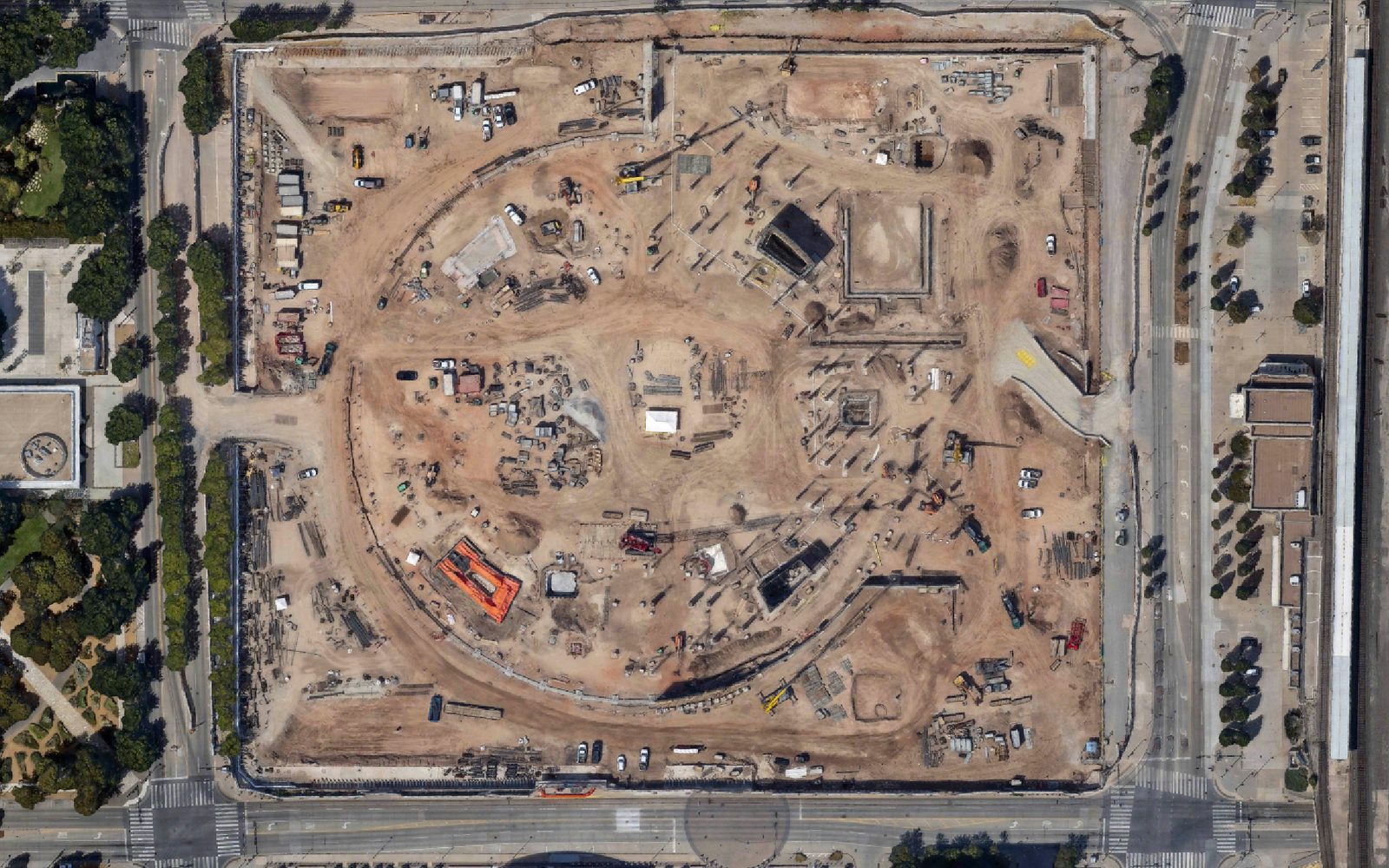 The same block on 2026-09-08 straight down from above: the building gone, the site excavated to its retaining walls, piling rigs and rebar cages across the floor, the arena on the way up