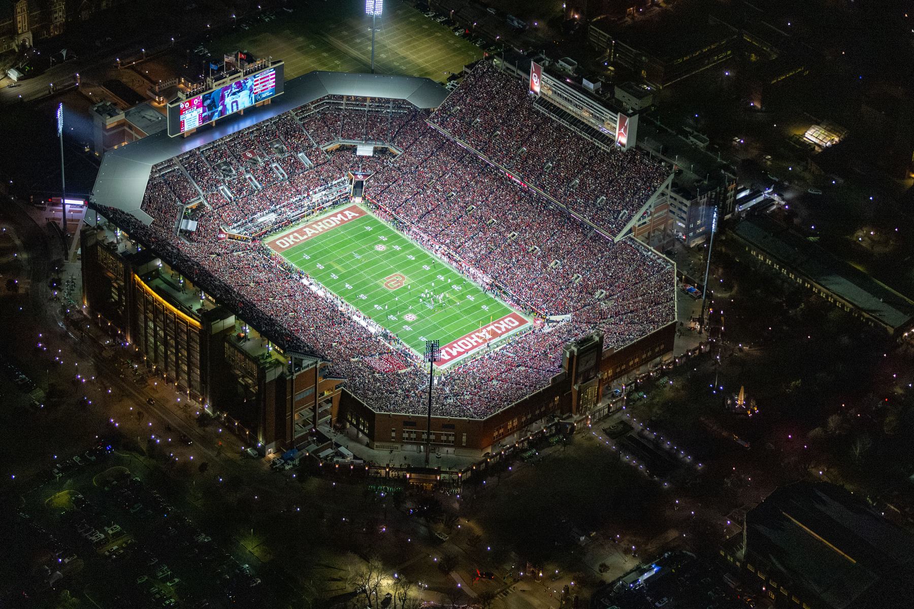 Memorial Stadium in Norman at night from the air, the stands full and the game under way